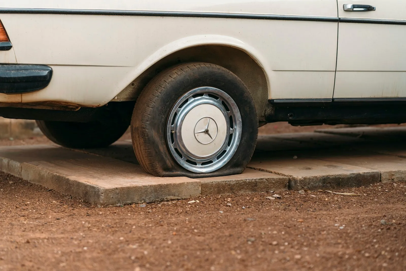Close-up of a flat front tire on an old white sedan parked on a concrete pad