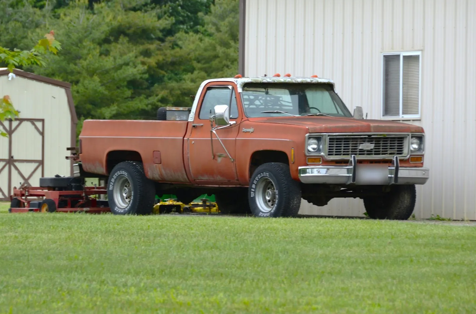 A faded red and white late 1970s Chevy pickup parked on grass beside a metal building